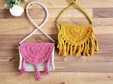 Zwei gehäkelte Umhängetaschen: rosa‑beige mit Quasten und senfgelb mit Fransen auf Holzuntergrund.
