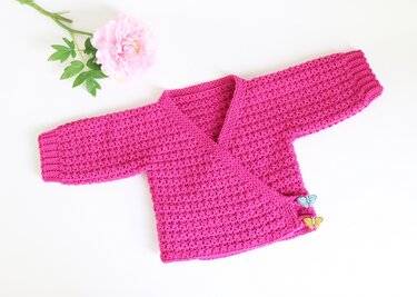 Gehäkelte pinke Wickeljacke für Babys mit Schmetterlingsknöpfen und rosa Blüte
