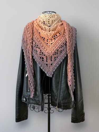 Gehäkeltes Dreieckstuch in Farbverlauf von Beige über Pfirsich zu Mauve mit filigranem Spitzenmuster, drapiert über einer schwarzen Lederjacke.
