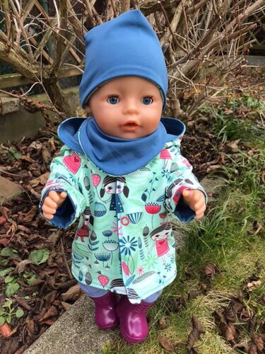 Puppe zeigt genähte Jacke mit Druckknöpfen, blaue Mütze, Halstuch und lila Stiefel