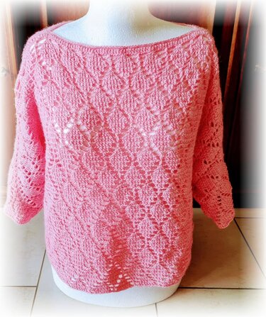 Rosa gehäkelter Pullover mit Rauten‑Lochmuster, U‑Boot‑Ausschnitt und Dreiviertelärmeln auf einer Schneiderpuppe.
