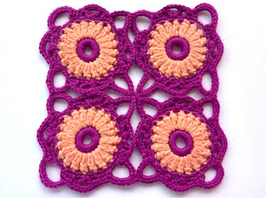 Viereckiges Häkelmotiv aus vier runden Blüten in Pfirsich und Magenta auf weißem Hintergrund