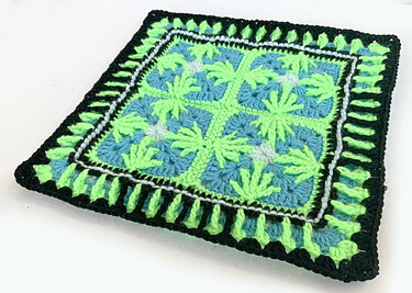 Gehäkeltes Quadrat in Neongrün, Hellblau und Schwarz mit palmenblattähnlichem Muster und gezacktem Rand.