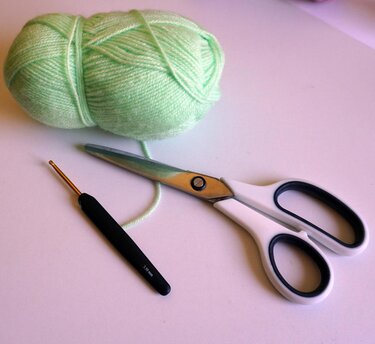 Light green yarn, 3.5 mm crochet hook, and scissors on a white background.
