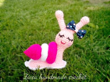 pink crocheted amigurumi snail with fuchsia shell coils and polka-dot bow
