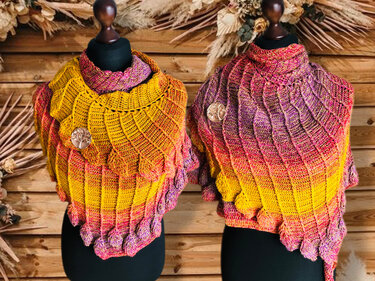 Zwei gehäkelte Tücher in Gelb, Pink und Lila mit Schuppenmuster und Baum-des-Lebens-Broschen vor Holzpaneelen.