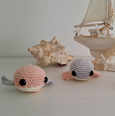 Zwei gehäkelte Amigurumi-Meerestiere in Pastell mit Flossen vor Muscheldeko