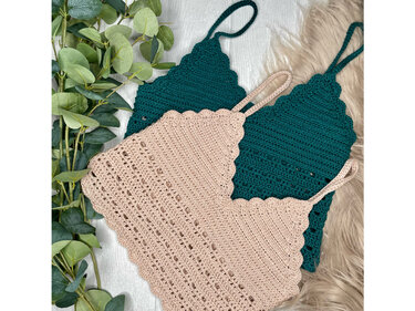 Zwei gehäkelte Damen-Tops in Beige und Dunkelgrün mit schmalen Trägern, auf hellem Untergrund mit grünen Blättern und flauschigem Stoff.