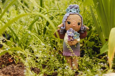 Gehäkelte Amigurumi-Puppe mit lila Haaren und Blumenstrauß in grünem Garten