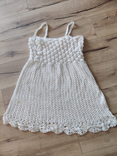 Weißes gehäkeltes Damenkleid mit dünnen Trägern, Noppenoberteil und Muschelsaum auf Holzfußboden