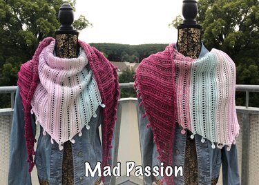 Gehäkeltes Dreieckstuch in Pink, Rosa, Hellblau und Weiß mit Lochmuster und Bommeln, drapiert über einer Jeansjacke.