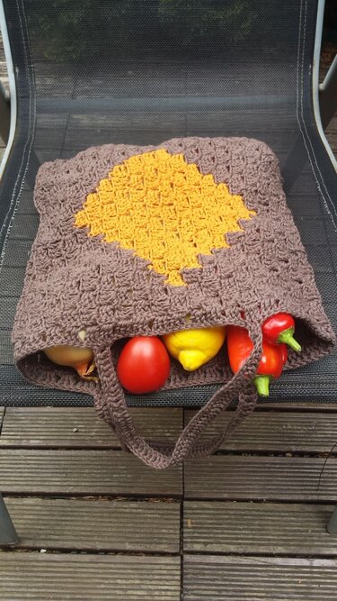 Gehäkelte braune Henkeltasche mit gelber Raute, gefüllt mit Tomate, Zitrone, Paprika und Zwiebel