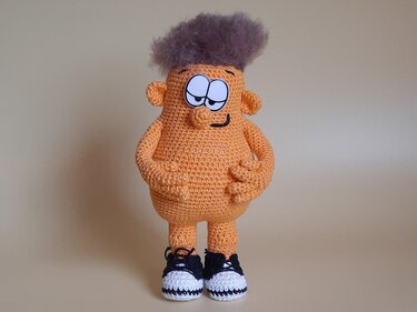 Orangefarbene Amigurumi-Figur mit grauen Wuschelhaaren und gehäkelten Turnschuhen