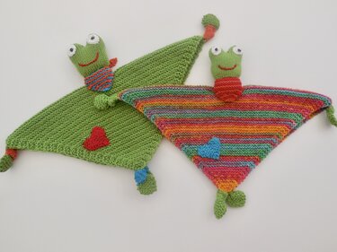 Zwei gestrickte dreieckige Schmusetücher mit Froschköpfen, eines grün, eines bunt gestreift, mit Herz-Applikationen und Knoten an den Ecken
