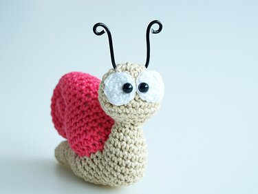 Gehäkelte Amigurumi‑Schnecke beige mit rosa Schneckenhaus und Drahtantennen