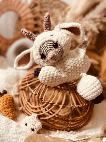 Weißes gehäkeltes Zicklein-Amigurumi mit Hörnern auf Weidenkorb, daneben Karotte und Stern