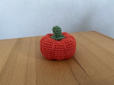 Oranger gehäkelter Mini-Kürbis mit grünem Stiel auf Holz.