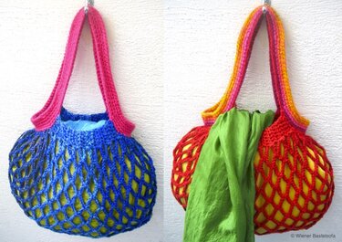Zwei gehäkelte Netztaschen in Blau und Rot mit farbigen Henkeln, an einer hellen Wand hängend; gelber Inhalt sichtbar, grünes Tuch in der roten Tasche.