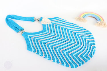 Crocheted blue chevron shoulder bag with metal clasp and cream appliqué on white background
