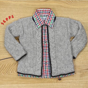 Graue gestrickte Kinderjacke mit Zopfmuster und schwarzer Borte, offen über kariertem Hemd