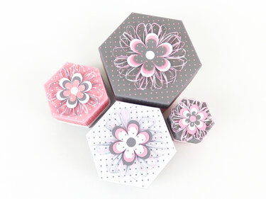 Set aus vier DIY-Hexagon-Geschenkboxen mit gestapelten Papierblumen und gepunktetem Muster