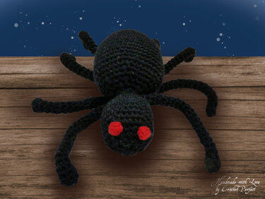 Schwarze gehäkelte Spinne mit roten Augen auf Holzplanken vor dunklem Himmel