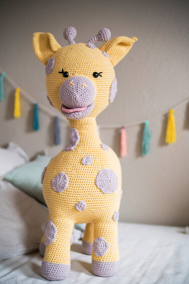 Gehäkelte gelbe Amigurumi-Giraffe mit lila Punkten und freundlichem Gesicht