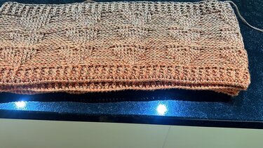 Nahaufnahme eines gehäkelten Loop-Schals mit Ombré-Verlauf in Orange- und Beigetönen und deutlich sichtbarem Strukturmuster.