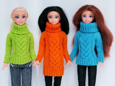 Drei Puppen in gestrickten Rollkragenpullovern mit Zopfmuster in Grün, Orange und Türkis