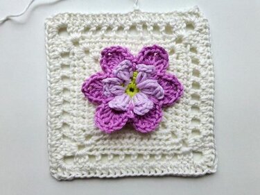 Weiße Granny-Umrandung mit zweilagiger lila Blüte und grünem Mittelpunkt