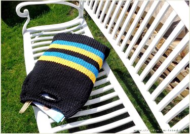 Schwarze Stricktasche mit blauen und gelben Streifen auf weißer Gartenbank