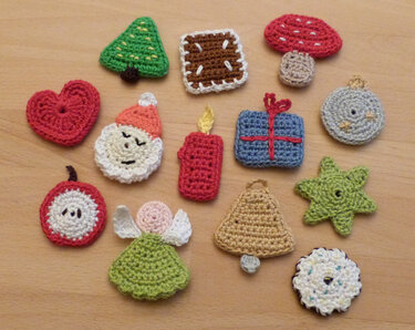 Mehrere kleine gehäkelte Weihnachtsmotive auf hellem Holz: Tanne, Geschenk, Kerze, Engel, Glocke, Herz, Pilz, Stern, Kugel und Keks