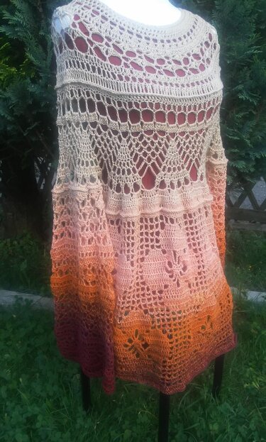 Gehäkelte Tunika mit Farbverlauf von Beige zu Rostrot und durchbrochenen Mustern auf einer Schneiderpuppe vor grünem Hintergrund