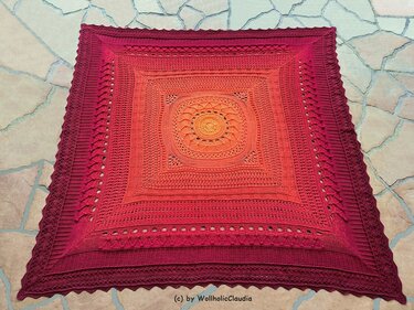 Quadratische Häkeldecke in Orange bis Dunkelrot mit Mandala-Motiv auf hellem Boden