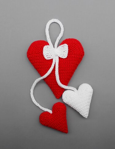 Drei gehäkelte Herzen in Rot und Weiß mit weißer Schleife und Aufhängung