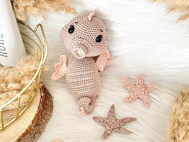 Gehäkeltes Amigurumi-Seepferdchen in Rosé mit zwei gehäkelten Seesternen auf hellem Untergrund
