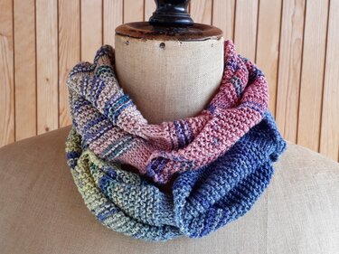 Knitted kids infinity cowl in pastel pink, blue and green stripes on a mannequin