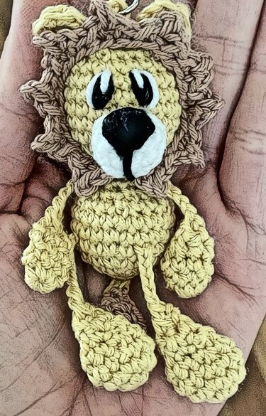 Hand hält kleinen gehäkelten Amigurumi-Löwen mit Mähne und Schlüsselring