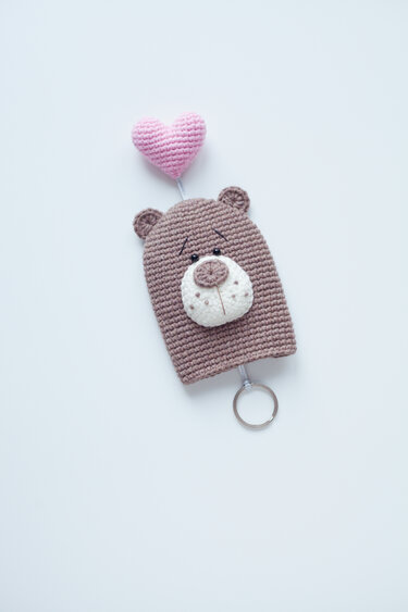 Brown crocheted bear keychain with white muzzle, embroidered eyes, and a pink heart balloon attached to a metal key ring