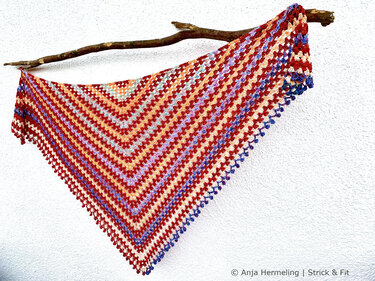 Striped granny-stitch triangle shawl in red, orange, purple and blue on a branch