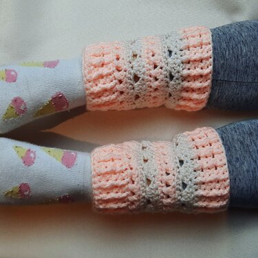 Gehäkelte rosa-creme Stulpen an Beinen, getragen über Socken mit Eismotiv und grauen Leggings