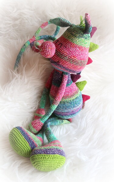 Gehäkeltes gestreiftes Amigurumi-Monster in Pink, Grün, Blau und Lila auf hellem Stoff