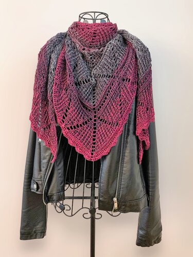 Fuchsia-to-grey ombre crocheted triangular shawl with openwork stitches, draped over a black leather jacket on a mannequin.