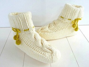 Cremefarbene gestrickte Hausschuhe mit Zopfmuster und limettengrünen Bommeln