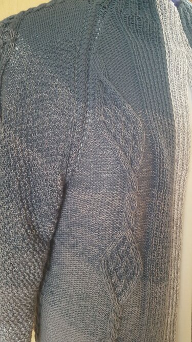 Nahaufnahme einer grauen Damenstrickjacke mit seitlichem Zopfmuster und Blattmotiven
