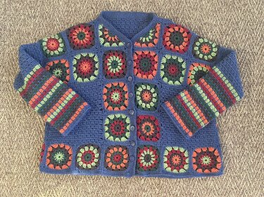 Vintage-inspirierte Häkeljacke aus bunten Granny-Squares auf blauem Grund
