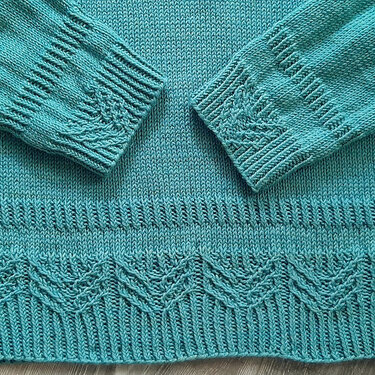 Nahaufnahme eines türkisen Strickpullovers mit Rippen-, Zopf- und Wellenmuster an Bündchen und Saum.