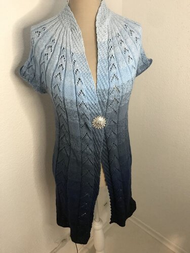 Damen-Strickweste mit blauem Farbverlauf, Ajourmuster, kurzen Ärmeln und Zierbrosche auf einer Schneiderpuppe
