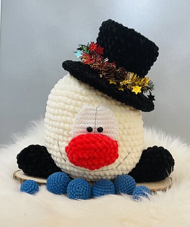 Gehäkelter Schneemannkopf mit roter Nase, schwarzem Zylinderhut und blauen Häkelbällen
