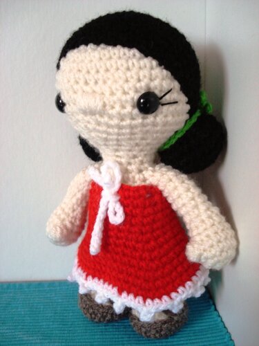 Amigurumi‑Puppe mit rundem Kopf, rotem Kleid und grünem Haarband